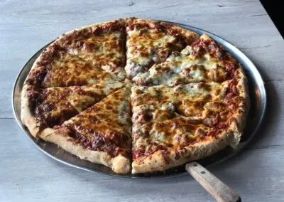Sliced pizza with bubbly cheese and meat on a metallic pan.