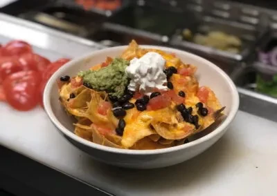 Nachos with melted cheese, black beans, tomatoes, guacamole, and sour cream.