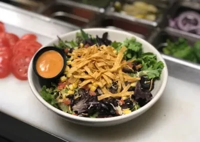 Vibrant salad bowl with greens, beans, corn, cheese, and tortilla strips.