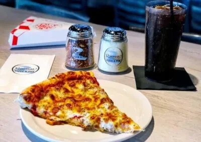 Pizza slice, soda, and shakers branded 'Riverside Pizza & Pub' on a table.