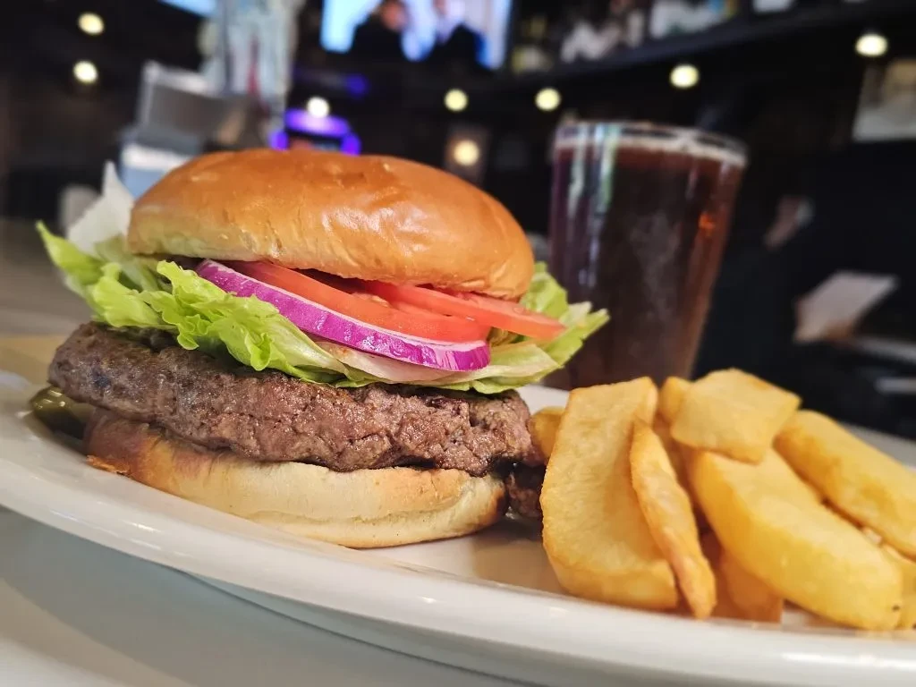 Close-up of a burger, fries, and drink on a plate in a restaurant.