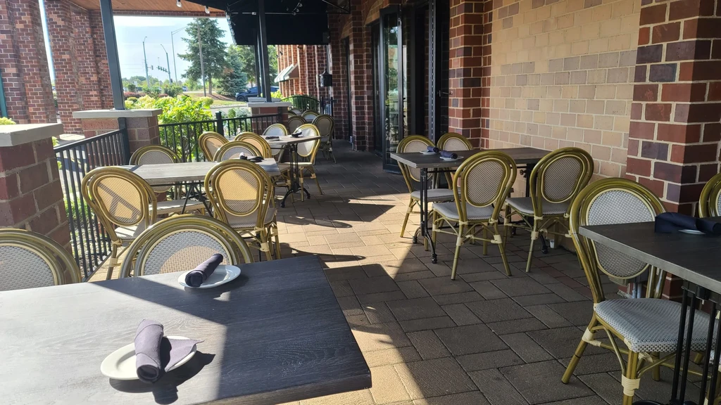 Sunny outdoor restaurant patio with set tables and rattan chairs.