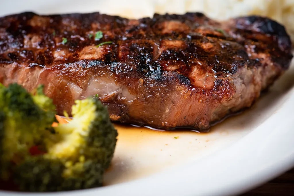 Close-up of a glistening, charred grilled steak with broccoli and rice.