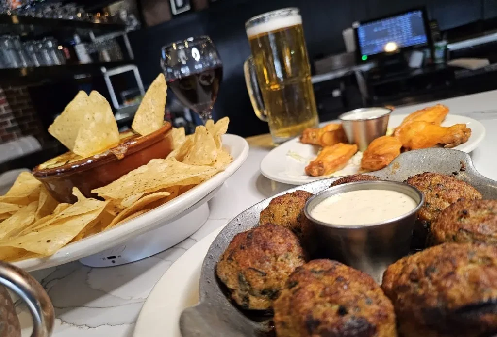 Fried appetizers, queso, wings, beer, and wine on a table.