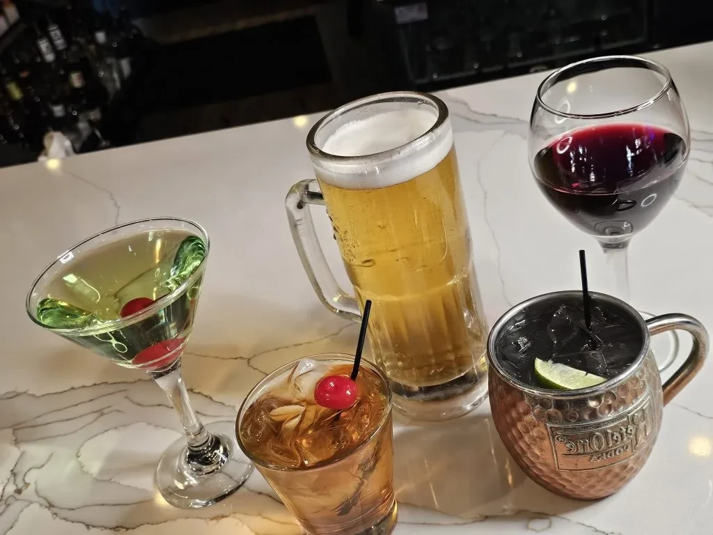 Five diverse alcoholic drinks: cocktails, beer, wine on a bar.