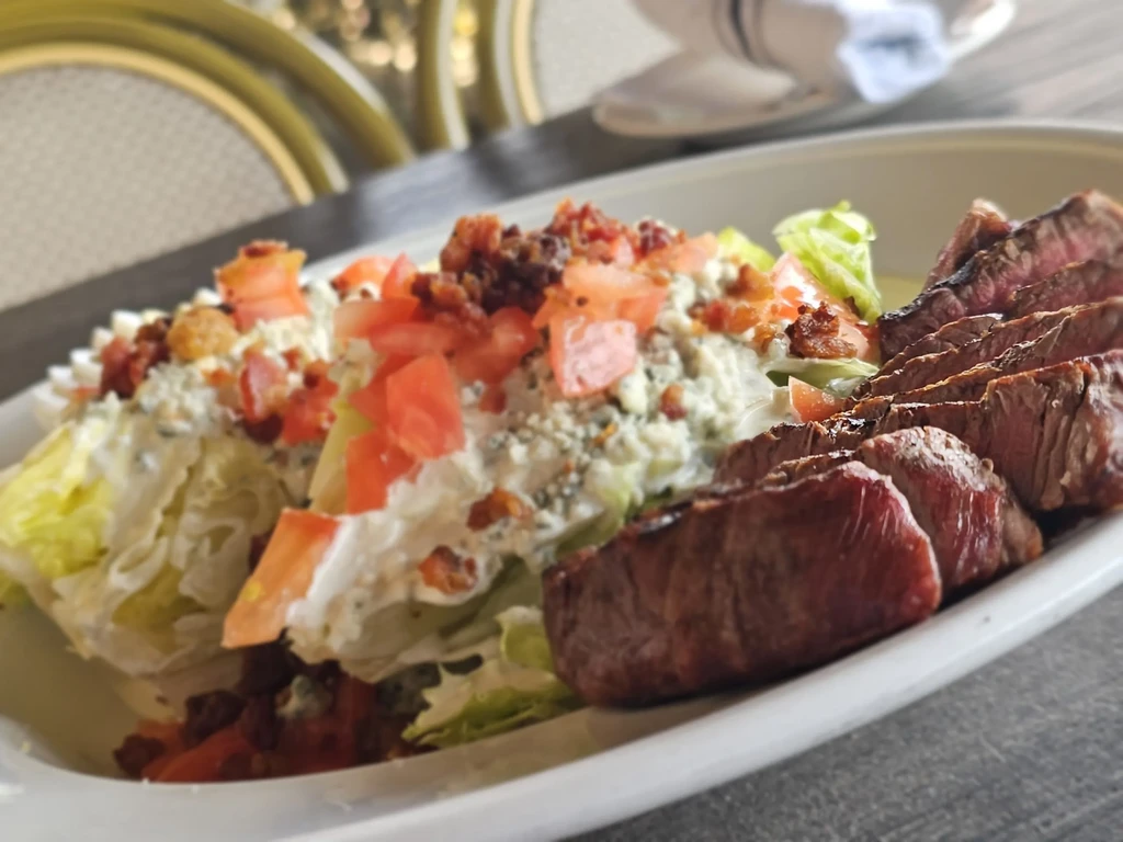 Sliced medium-rare steak and blue cheese wedge salad on a restaurant plate.
