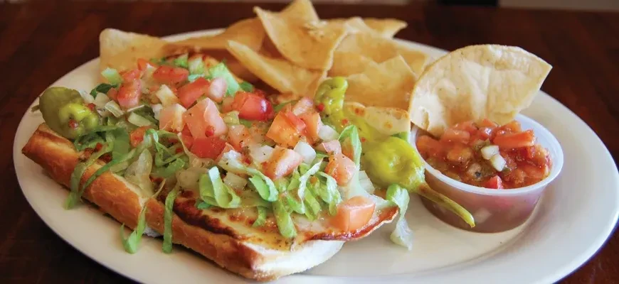 Open-faced sub with lettuce, tomato, onion, chips, salsa, and a pepperoncini.