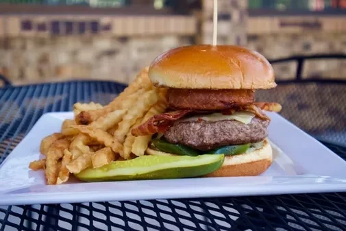 Gourmet burger with crinkle-cut fries and pickle on a white plate.