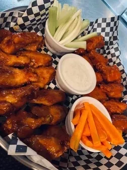 Buffalo wings, celery, carrots, and dip on a checkered tray.