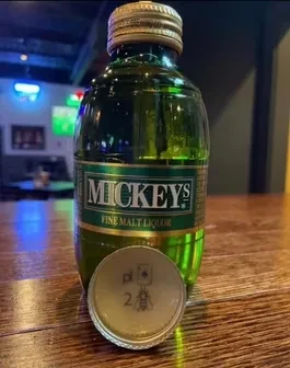 Green Mickey's Malt Liquor bottle with bee-2 cap on a bar.