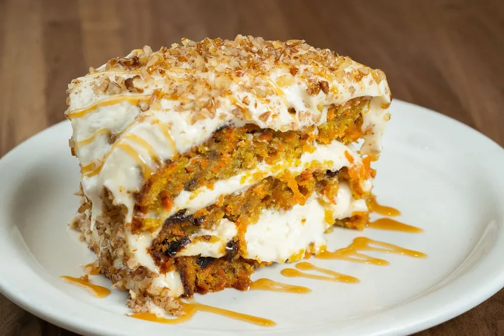 Layered carrot cake slice with frosting, nuts, and caramel drizzle.