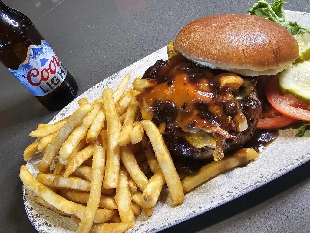 Close-up of a sauced burger, fries, salad, and Coors Light beer.