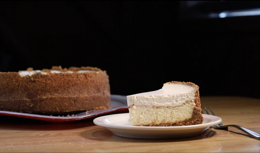 Slice of layered cheesecake on a white plate with a fork.