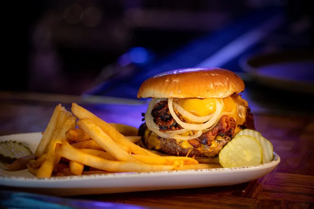 Burger with melted cheese, onions, golden fries, and pickles on a plate.