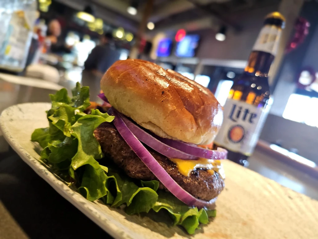 Close-up hamburger, cheese, lettuce, onion; blurred Miller Lite in restaurant setting.