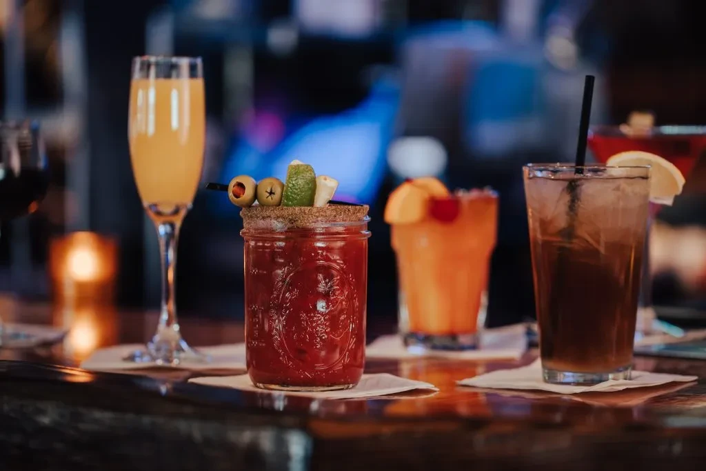 Five different cocktails and drinks on a reflective bar counter.