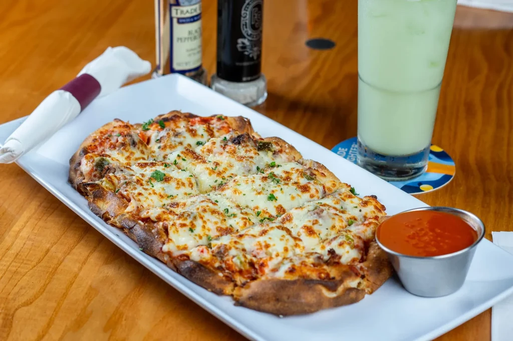 Close-up of cheesy flatbread, red sauce, green drink on wooden table.