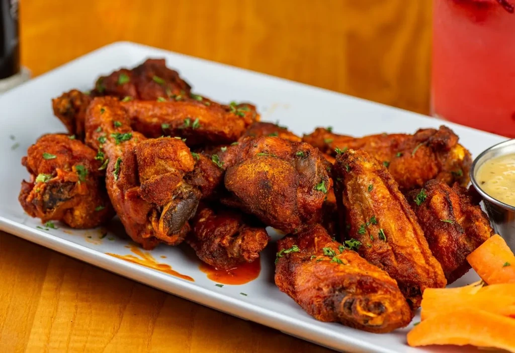 A plate of crispy, saucy chicken wings with dip and carrots.