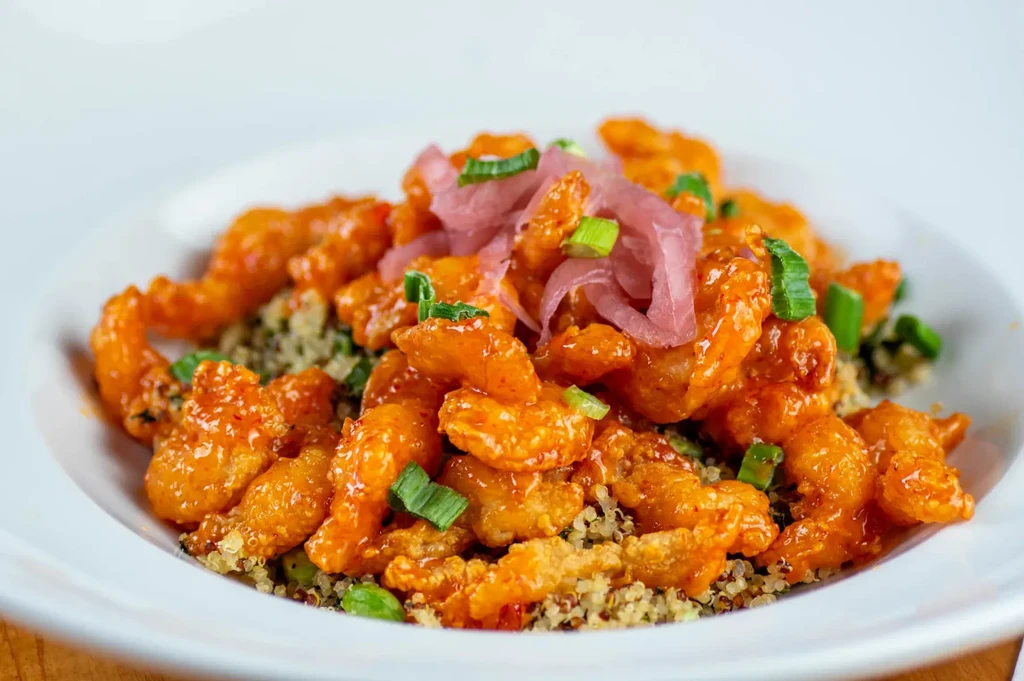 Reddish-orange glazed fried protein on quinoa, with pickled red and green onions.