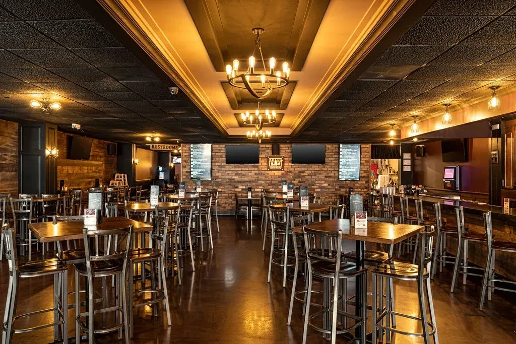 Empty rustic-industrial bar dining area with high-top tables and chandeliers.