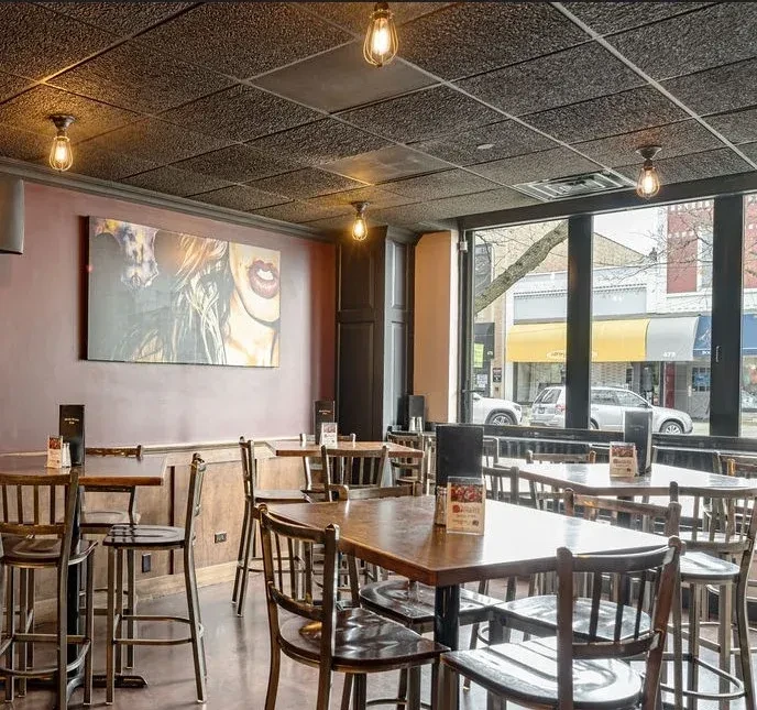 Empty restaurant with dark wood tables, purple walls, modern art, street view.