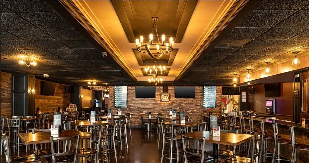 Empty rustic-industrial restaurant with chandeliers, dark wood, and brick walls.