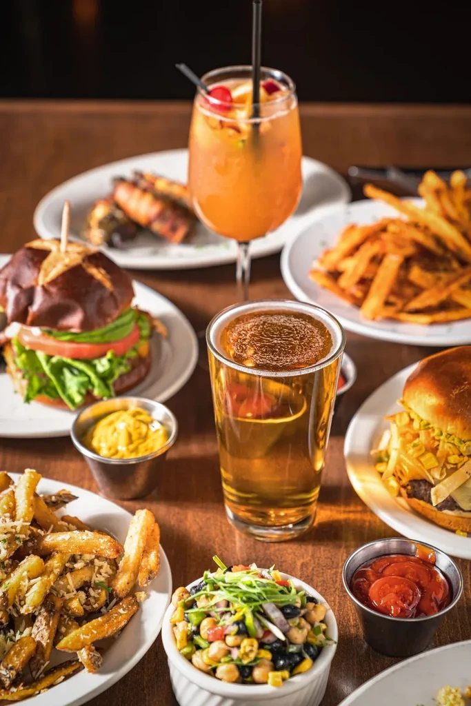 Two gourmet burgers, fries, cocktail, and beer on a restaurant table.