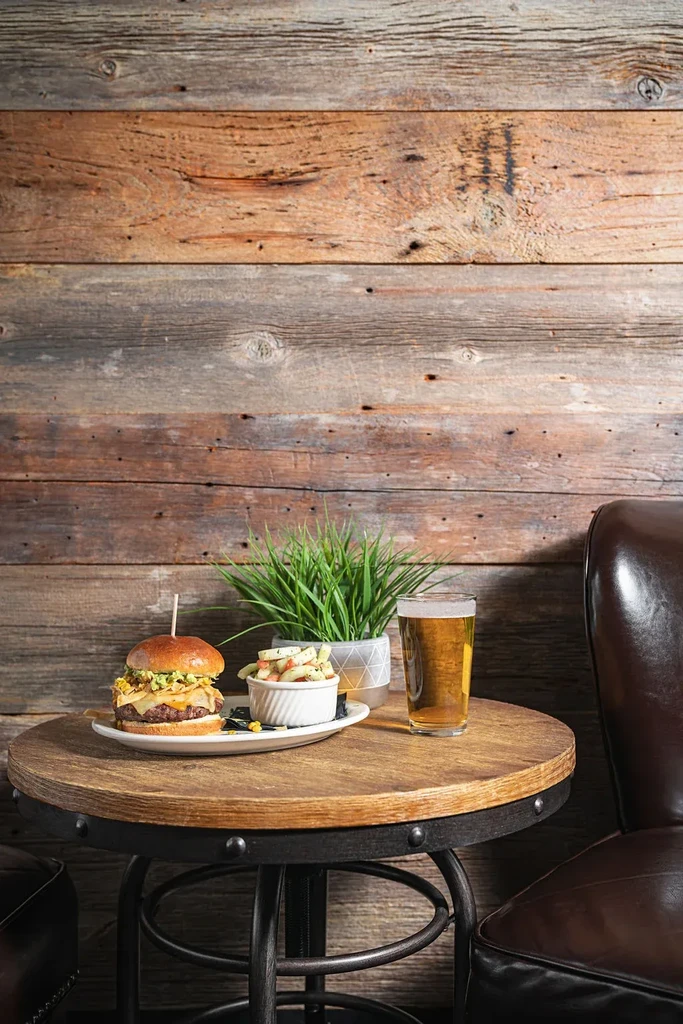 Gourmet burger with guacamole, beer, and a side on a wooden table.