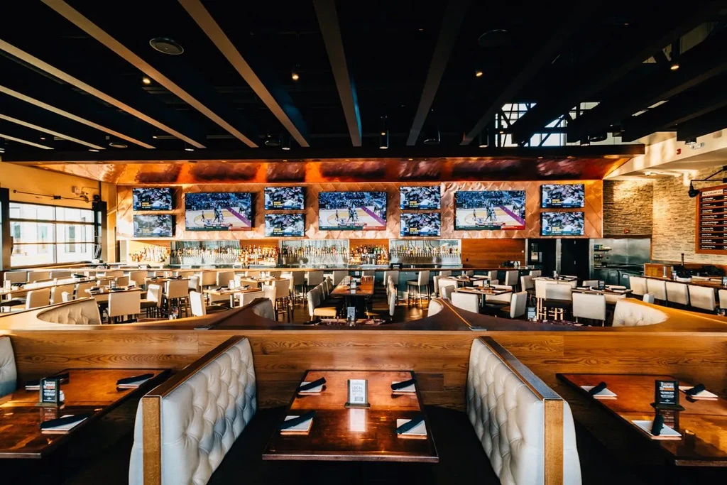 Modern restaurant interior with large bar and TVs showing basketball.