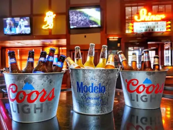 Three branded buckets of beer and ice in a busy bar.