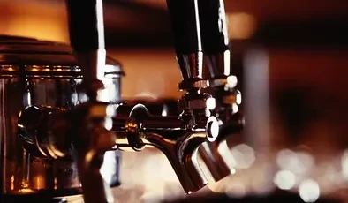Polished metal beer taps reflect warm light in a dimly lit bar.