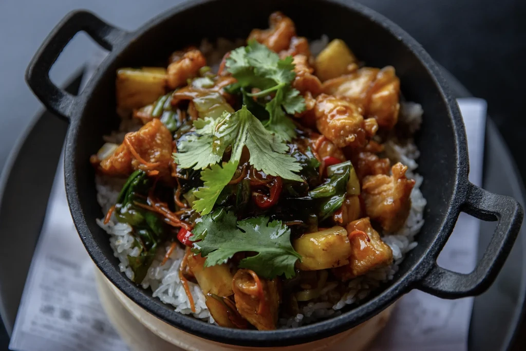 Rice bowl with chicken, pineapple, vegetables, and cilantro in a dark pot.