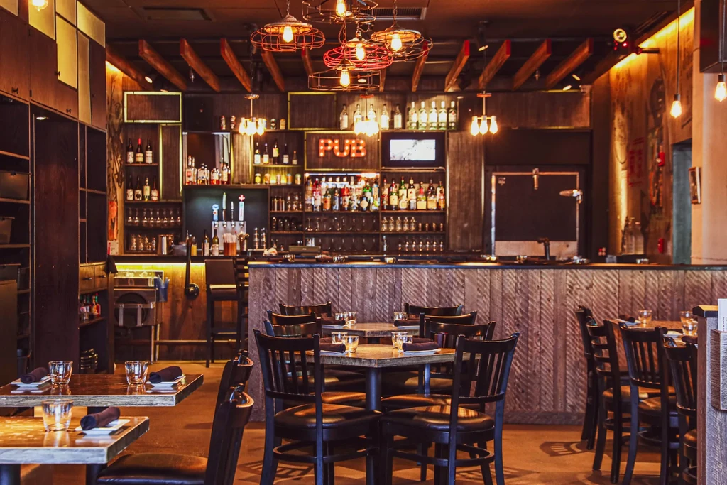Warmly lit pub interior with a well-stocked bar and set tables.