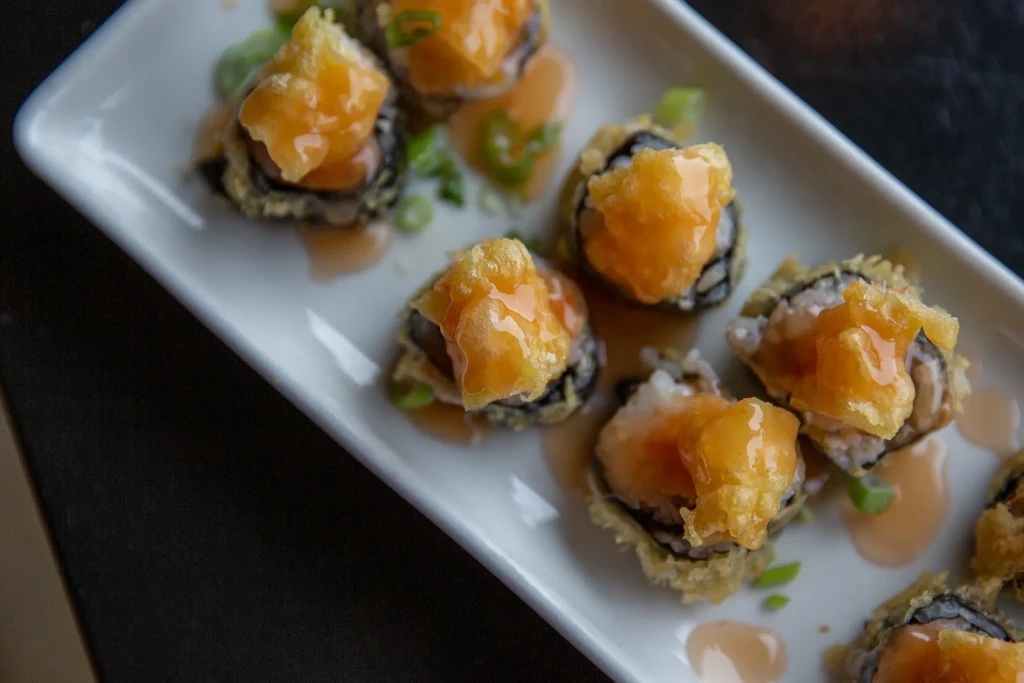 Tempura sushi rolls with creamy orange sauce, green onion on white plate.