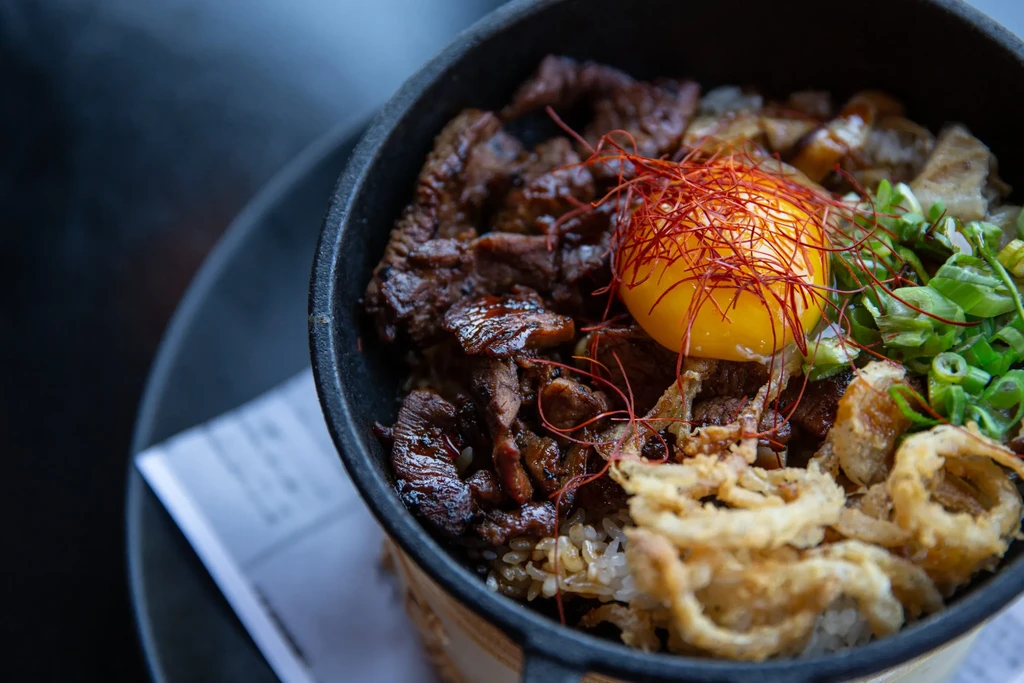 Rustic bowl with rice, glazed meat, egg yolk, scallions, and chili thread.