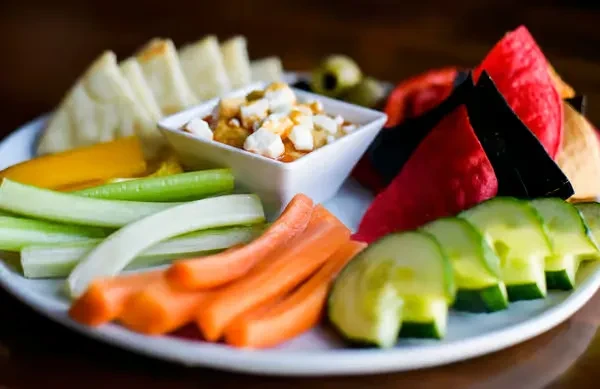 Colorful appetizer platter with dip, feta, vegetables, pita, and chips.