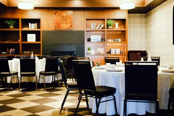 Restaurant dining room with white-set tables, checkered floor, and wooden paneling.
