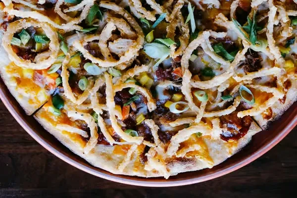 Gourmet pizza with crispy onions, shredded meat, and mixed vegetables.
