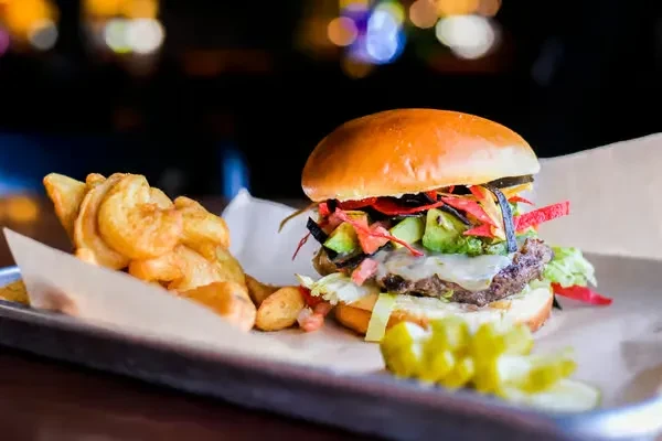 Gourmet burger with avocado, tortilla strips, and fries on a tray.
