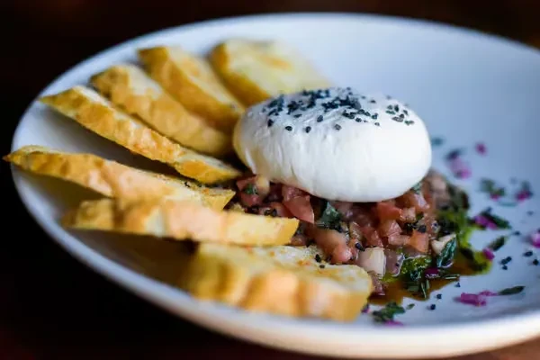 Close-up of burrata with sesame, diced tomatoes, herbs, and baguette.