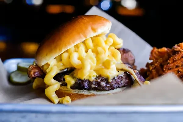 Gourmet burger topped with macaroni and cheese, bacon, and pickles.