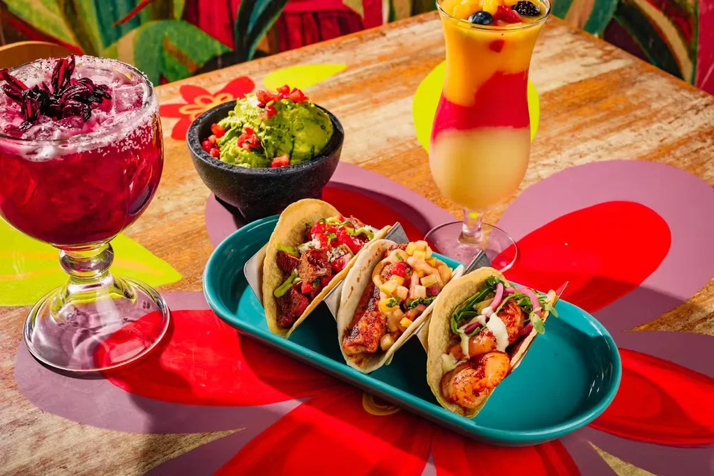 A vibrant display of drinks, tacos, and guacamole on a decorated table.