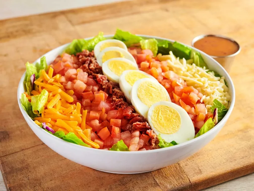 Colorful salad with lettuce, cheddar, tomatoes, bacon, and sliced eggs.