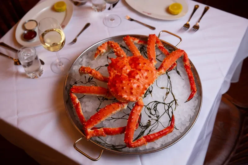 Bright orange cooked king crab on ice with wine and sauces.