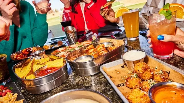 People interacting around a table with appetizers and drinks.