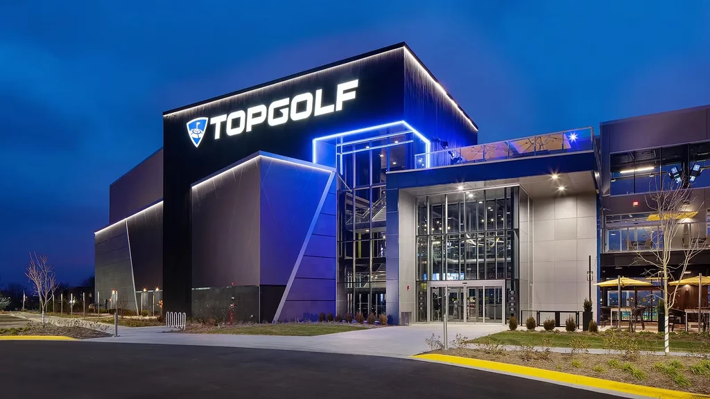 Modern TOPGOLF building exterior at dusk with blue and warm lights.