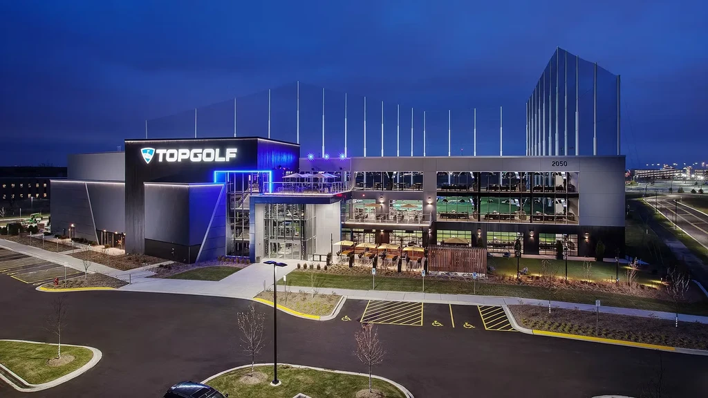 Illuminated multi-story Topgolf building and golf driving range at twilight.