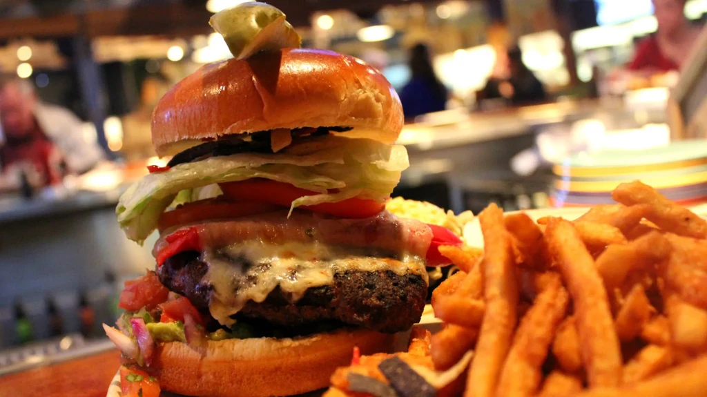 Stacked gourmet burger with melted cheese, fries, and pickle spear.