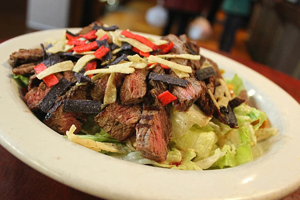 Medium-rare sliced steak salad with colorful tortilla strips.