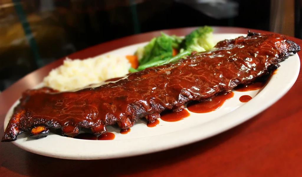 Rack of dark-sauced barbecue ribs with mashed potatoes and green vegetables.